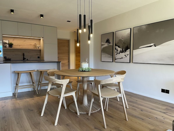 Ein moderner Essbereich mit einem runden Holztisch, sechs Holzstühlen, Pendelleuchten und gerahmten Kunstwerken an den Wänden.