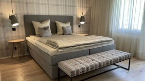 Ein modernes Schlafzimmer mit einem großen Bett, Nachttischen, einer Bank und einer Wand mit Karomuster.