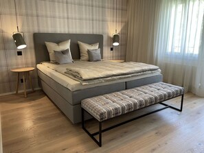 Ein modernes Schlafzimmer mit einem großen Bett, Nachttischen, einer Bank und einer Wand mit Karomuster.