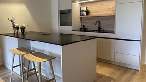 Eine moderne Küche mit einer zentralen Kochinsel, Holzstühlen, einem Einbauofen und einer Holzrückwand.