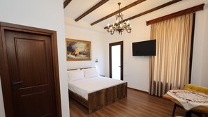 A bedroom with a wooden bed, a painting, a TV, and a yellow chair. - VillaStarova (Berat)