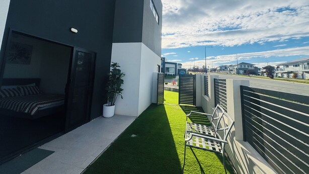 Un edificio moderno con balcón, un pequeño jardín y vista a la calle.