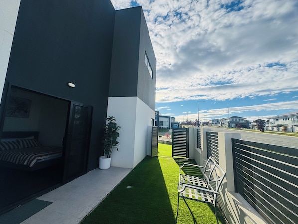 A modern building with a balcony, a small garden, and a view of the street.