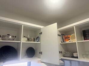 Una cocina con alacenas abiertas, que contiene utensilios de cocina, platos y un escurreplatos.