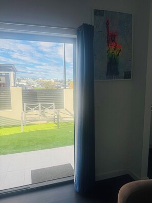 A room with a large sliding glass door leading to a balcony, a painting of a statue, and a view of a cityscape. - Bright and Cozy suite for 4 guest, feel like a home with Molonglo valley views (Whitlam)