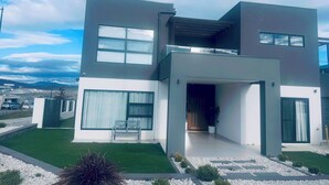 Una casa moderna de dos pisos con techo plano, ventanas amplias y un césped bien cuidado.