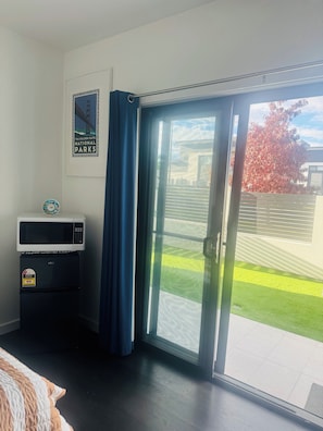 A room with a bed, a microwave, a refrigerator, a poster of the Golden Gate National Parks, and a sliding glass door leading to a green lawn.