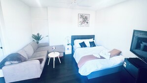 Un dormitorio con cama, sofá, una mesita, mesita de noche, ventilador de techo y televisión.