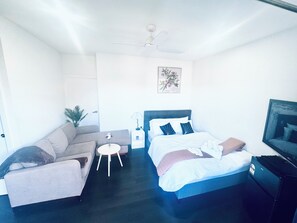 A bedroom with a bed, a sofa, a small table, a nightstand, a ceiling fan, and a TV. - Bright and Cozy suite for 4 guest, feel like a home with Molonglo valley views (Whitlam)
