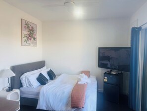 Una habitación de hotel con cama, televisión, escritorio y ventilador de techo.