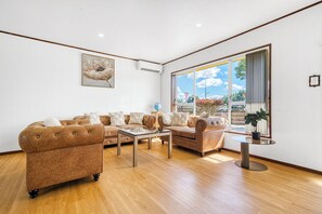 A spacious living room with a large window, a sofa set, a coffee table, and a small side table. - Warmth and the spacious 2 double bedroom (Manurewa)