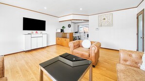 Een moderne woonkamer met een flatscreen televisie, een bank, een salontafel en een keuken in de achtergrond.