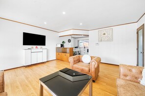 A modern living room with a flat-screen TV, a sofa, a coffee table, and a kitchen area in the background. - Warmth and the spacious 2 double bedroom (Manurewa)