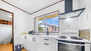 Een kleine keuken met witte kastjes, een fornuis en een raam met uitzicht op een woonwijk.