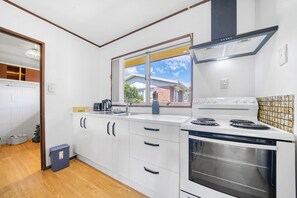 A kitchen with white cabinets, a stove, and a window. - Warmth and the spacious 2 double bedroom (Manurewa)