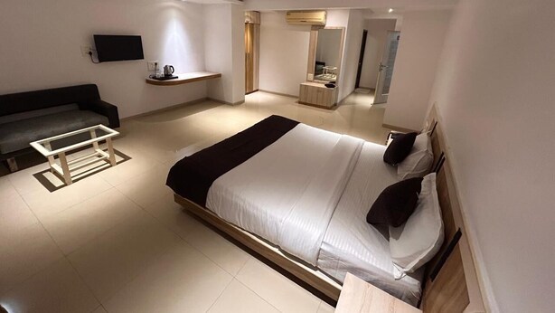 A modern bedroom with a large bed, a sofa, a TV, and a ceiling fan. - The Neelam Executive (Rajgurunagar)