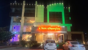 A building with a sign that reads 'द निलम एखिस्क्रूइंट' and two cars parked in front. - The Neelam Executive (Rajgurunagar)