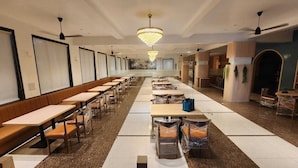 A long corridor with rows of tables and benches, a chandelier, and ceiling fans. - The Neelam Executive (Rajgurunagar)
