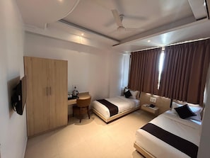 A hotel room with two beds, a desk, a wardrobe, and a television.