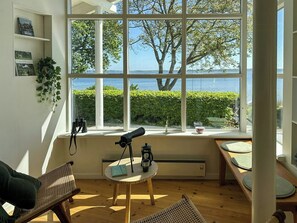 Una habitación con un ventanal grande, un telescopio, una mesa y una silla.
