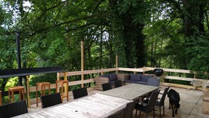 Una terraza de madera con una mesa de comedor y sillas, un sofá y una parrilla.