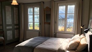Un dormitorio con una cama, dos ventanas, un radiador y una lámpara.