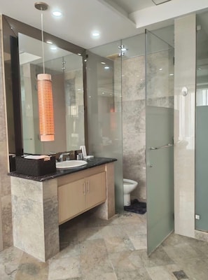 A modern bathroom with a marble vanity, a large mirror, a glass shower enclosure, and a hanging light fixture.