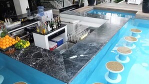 Zona de bar junto a la piscina con encimera de mármol, exhibición de frutas y varios taburetes.