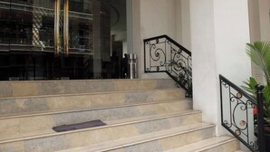Unos escalones de piedra conducen a una escalera de hierro forjado negro con barandilla.