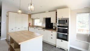 Una cucina moderna con mobili bianchi, un piano di lavoro in legno, elettrodomestici in acciaio inossidabile, luci a sospensione e una finestra con persiane.