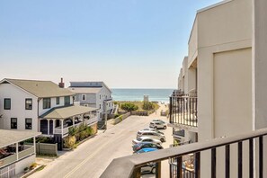 A coastal residential street with houses, a beach, and parked cars.