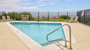 Une piscine rectangulaire dotée d’une rambarde de sécurité en métal, entourée de chaises longues et d’une clôture.
