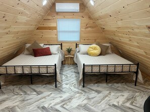 A room with two beds, wooden walls, a window, and an air conditioner.