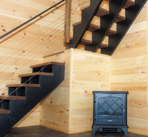 A wooden interior with a staircase, a black heater, and a wooden wall.