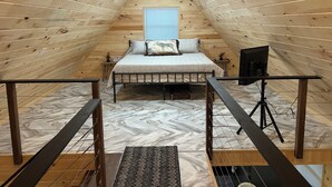 Una habitación con techo alto de madera, una cama, una mesita y un ventanal.