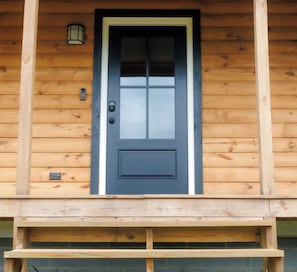 A wooden building with a dark blue door, a small light fixture above it, and a mailbox to the left.