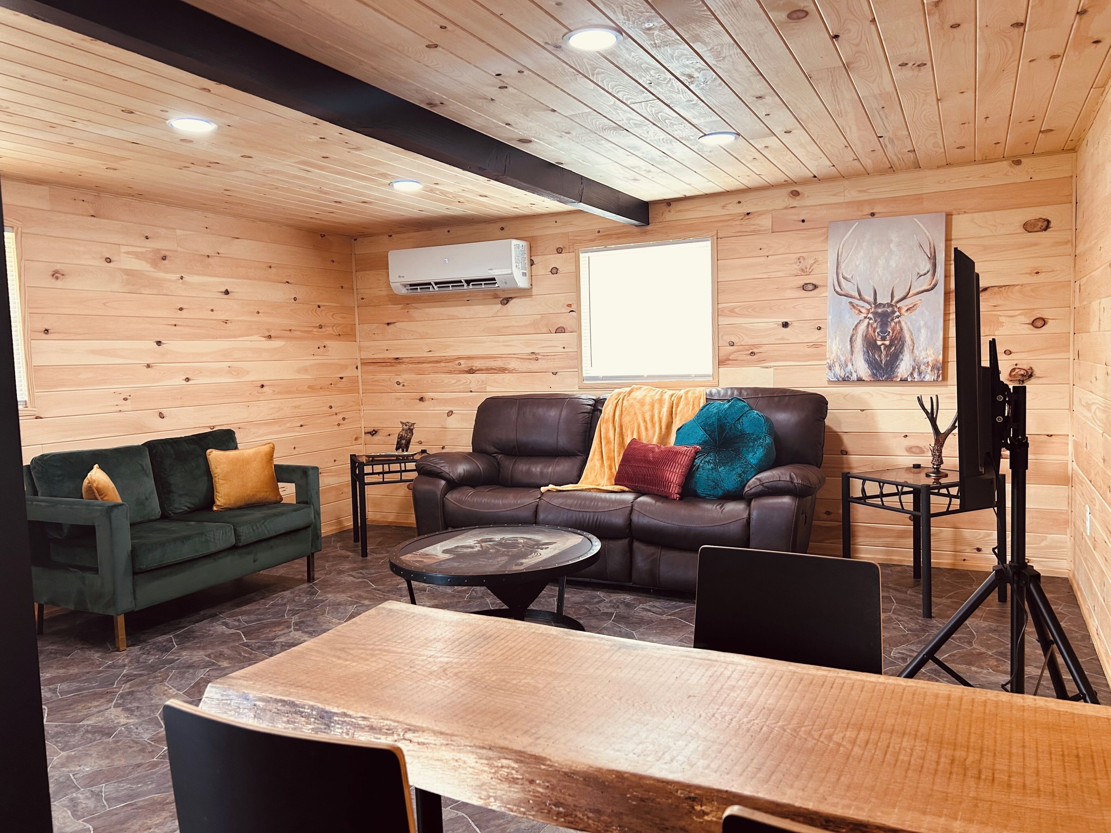 A cozy log cabin interior with a leather sofa, a green couch, a wooden dining table, and a mounted television.. The Lodge Cabin ~Norris Lake Views and Mountain Backdrops