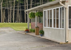 A building with a covered porch, brick foundation, and potted plants.