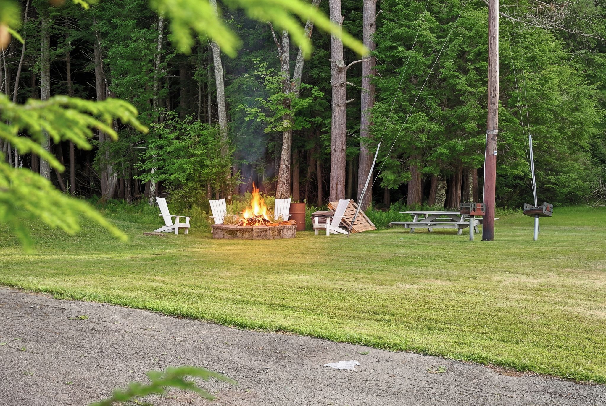 A campsite with a fire pit, picnic table, and chairs.