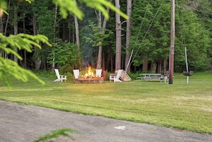 A campsite with a fire pit, picnic table, and chairs.
