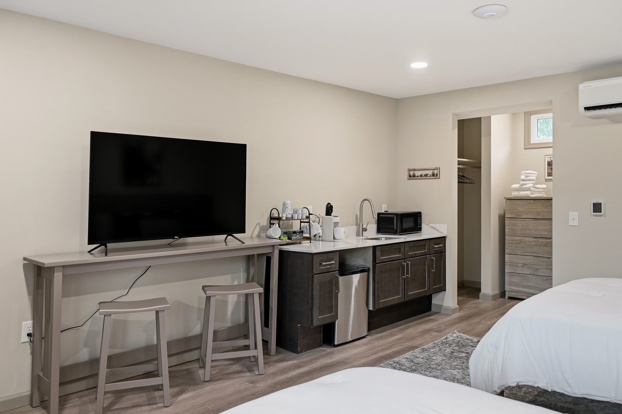 A compact hotel room with a kitchenette, a flat-screen TV, a small dining area, and a bed.