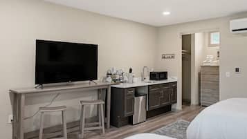 A compact hotel room with a kitchenette, a flat-screen TV, a small dining area, and a bed.