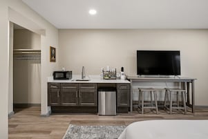 A compact kitchen with a microwave, sink, and a coffee maker, a dining area with a TV, and a visible trash bin.