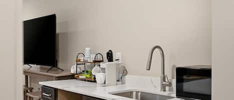 A modern kitchen with a flat-screen TV, a microwave, a sink, and a coffee maker.