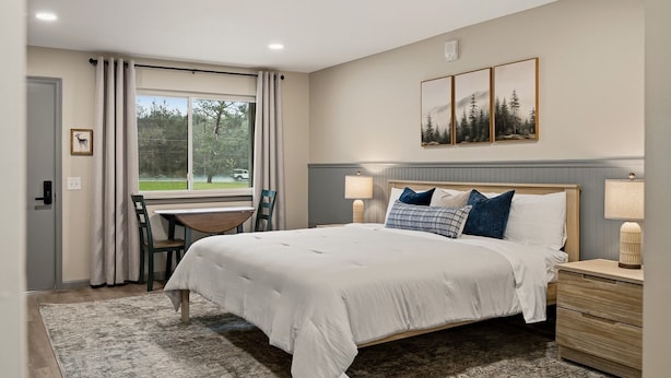 Une chambre à coucher avec un grand lit, des tables de chevet, un bureau et une fenêtre avec des rideaux.