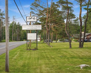 A sign for Sullivan Trail Inn & Suites with a clear view of the surrounding trees and a road. - Sullivan Trail Inn and Suites (Pocono Lake)