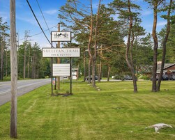 A sign for Sullivan Trail Inn & Suites with a clear view of the surrounding trees and a road.