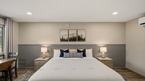 Une chambre d’hôtel avec un grand lit, deux tables de chevet avec des lampes, un bureau avec une chaise, une fenêtre avec des rideaux et un tableau accroché au mur.