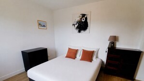 Un dormitorio con cama, dos almohadas, una mesita de noche, un aparador, una lámpara y una obra de arte en la pared.