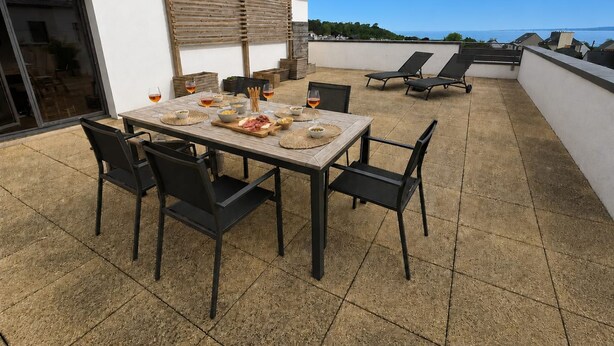 Una terraza en la azotea con una mesa lista para comer, sillas negras y vistas al mar.